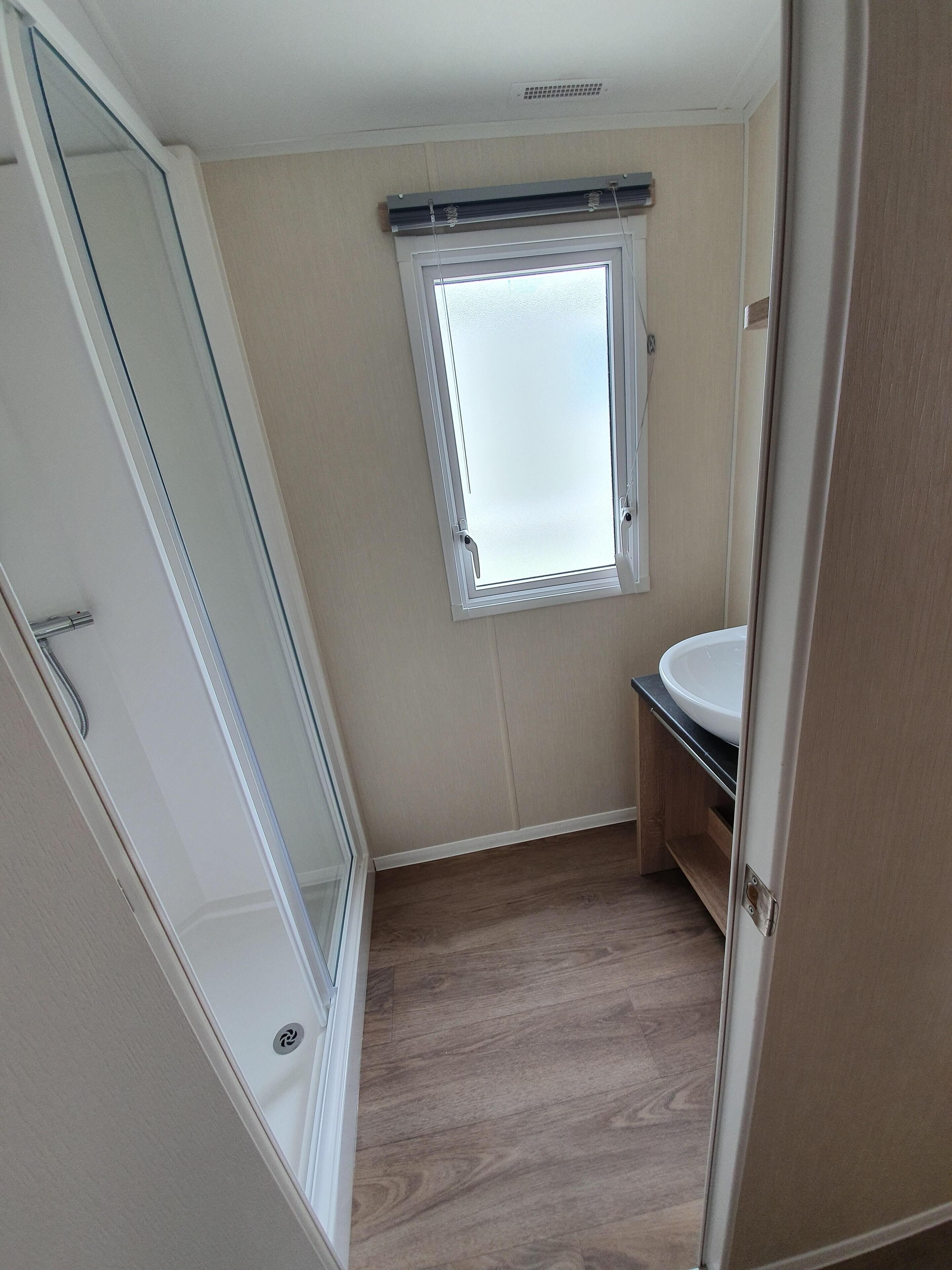 A small bathroom with a window, a sink, and a shower.