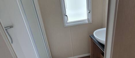 A small bathroom with a window, a sink, and a shower.
