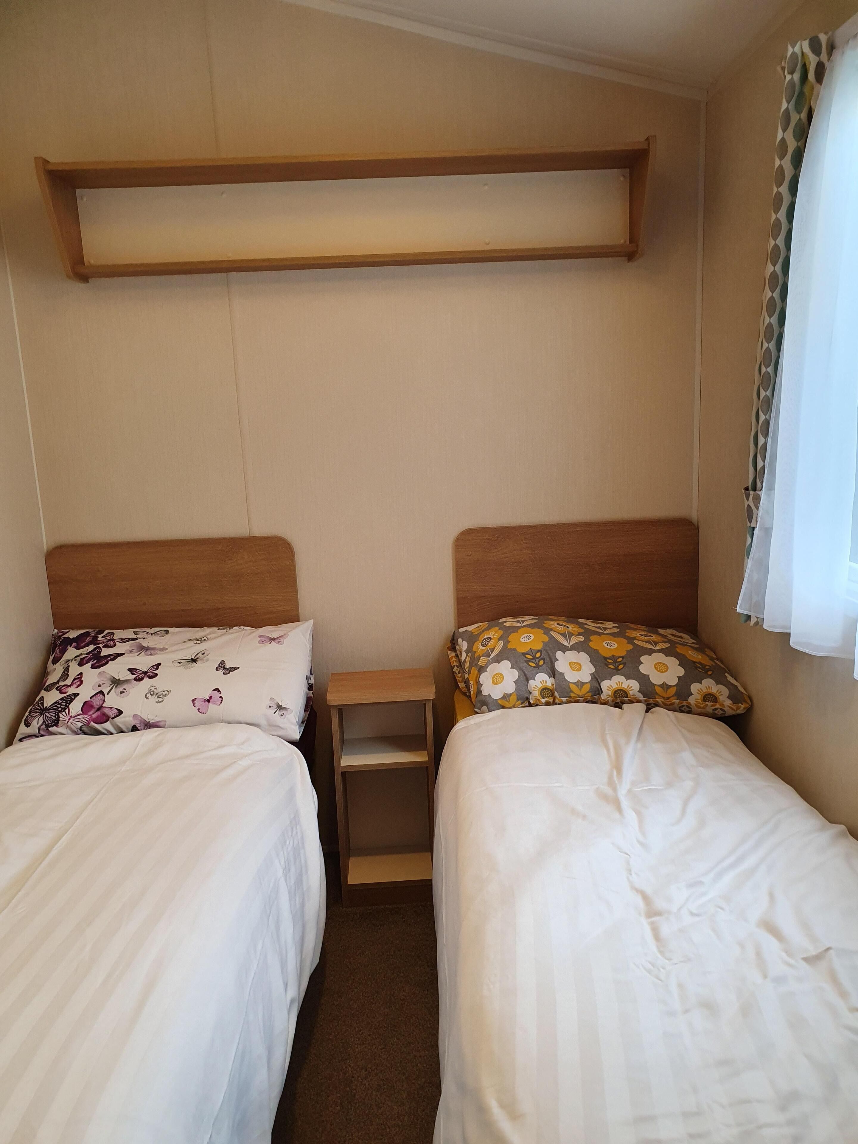 Ein Schlafzimmer mit zwei Einzelbetten, einem Holzregal darüber und einem kleinen Nachttisch.