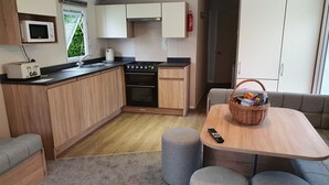 Eine kompakte Küche mit Mikrowelle, Toaster und Herd. Es gibt einen Essbereich mit Tisch und Poufs, und einen Korbwäscher auf dem Tisch.