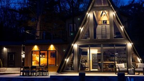 A modern house with a triangular roof, large glass windows, and a well-lit interior. - Lakewood Lux Property - Saugatuck Harbor Luxury A-Frame, View of Downtown (Saugatuck)