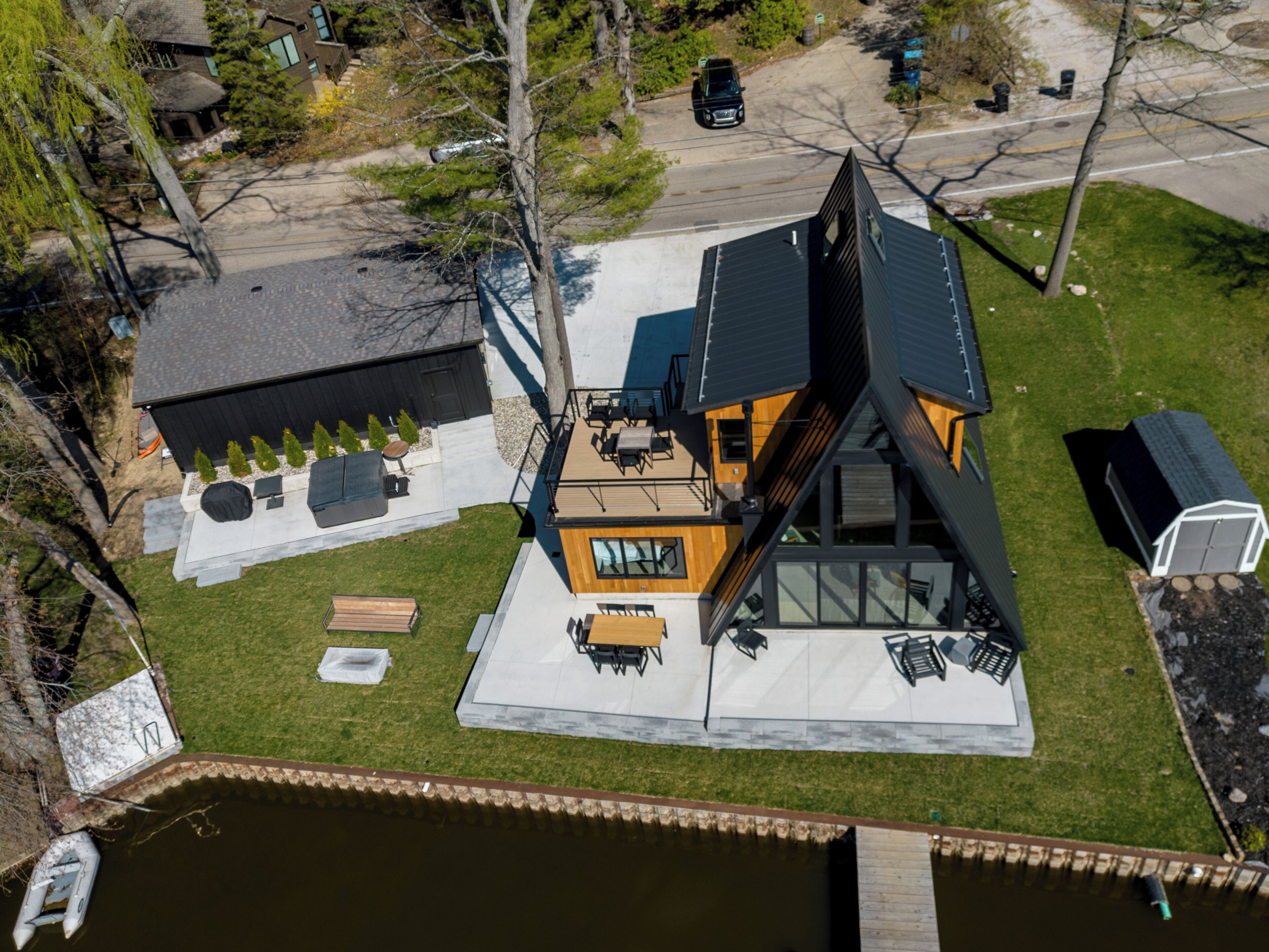 Uma casa moderna com um telhado triangular único, um pátio com móveis de exterior e um pequeno cais à beira da água.