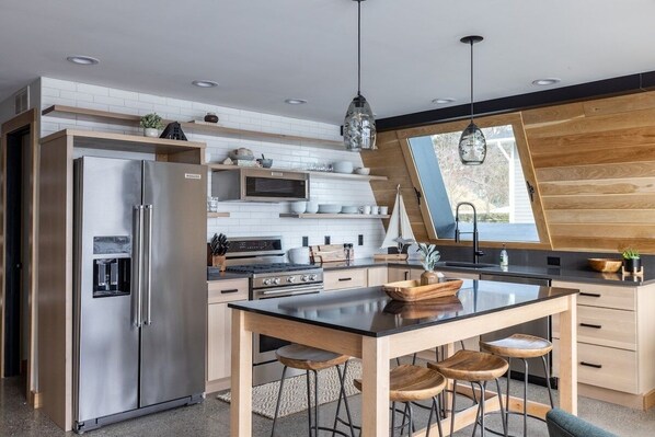 Una cocina moderna con refrigerador de acero inoxidable, horno empotrado e isla de madera con taburetes de bar.