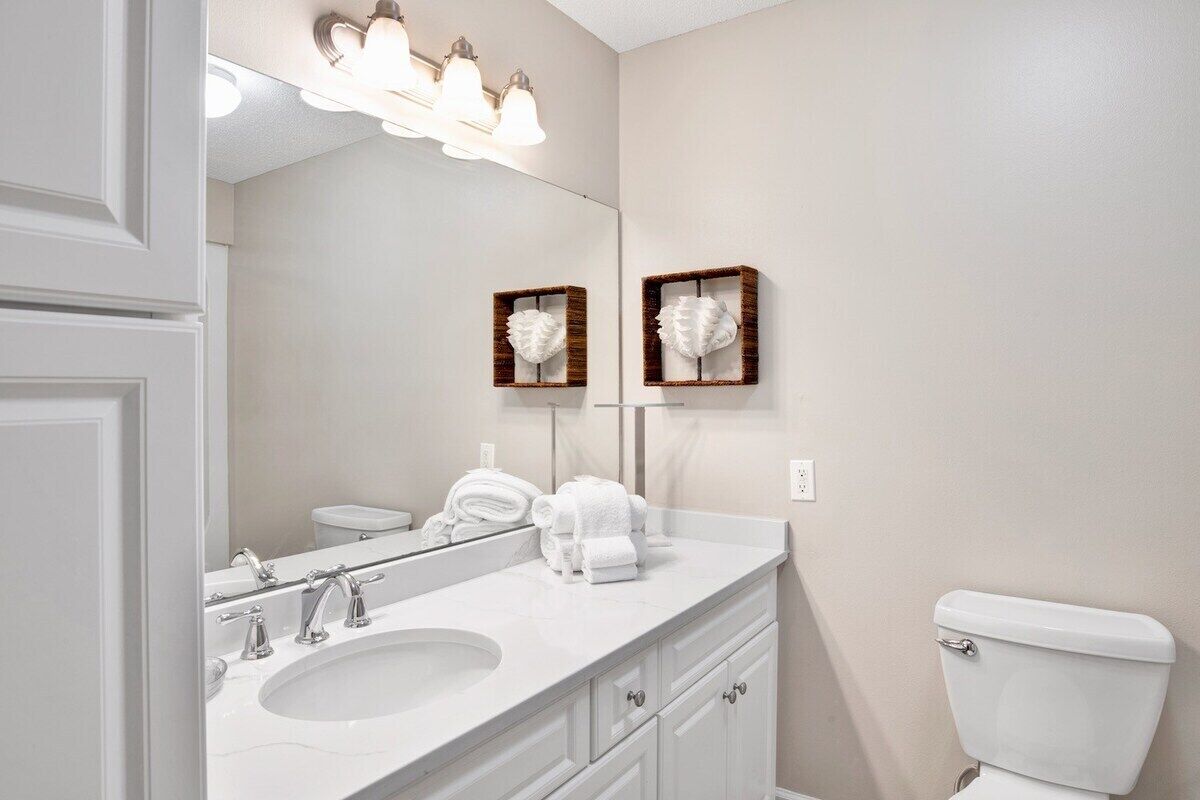 A bathroom with a white sink, two towel racks, a toilet, and a mirror with light fixtures above.