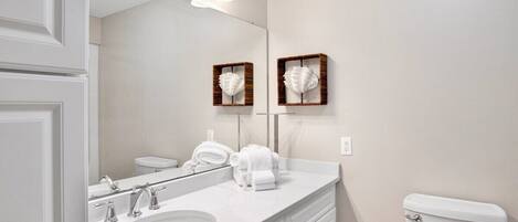 A bathroom with a white sink, two towel racks, a toilet, and a mirror with light fixtures above.