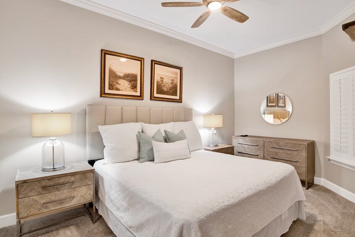 A bedroom with a bed, nightstands, a dresser, a ceiling fan, and framed pictures on the wall.