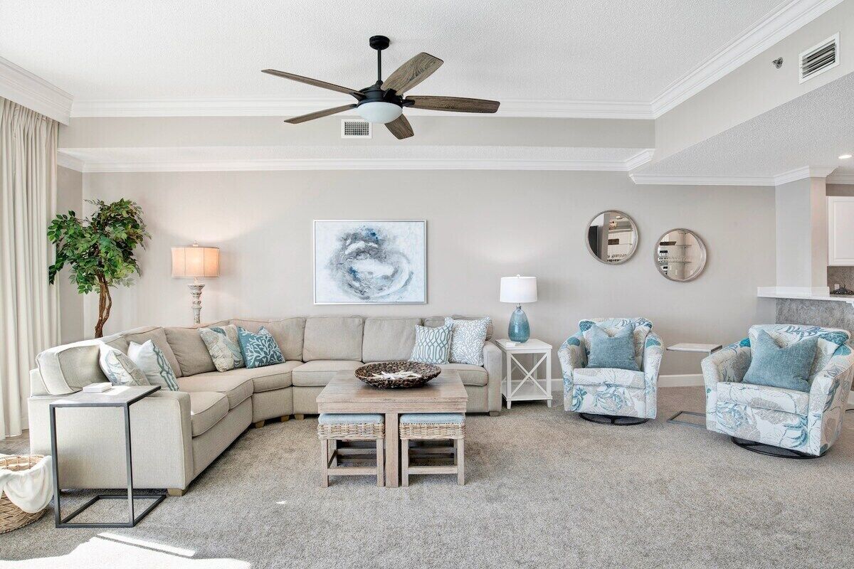 A living room with a sectional sofa, two armchairs, a coffee table, and a ceiling fan.