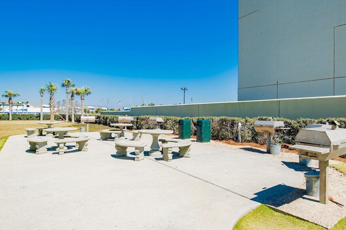 Outdoor seating with tables and benches, a barbecue grill, and a large building in the background.