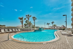A pool area with lounge chairs and palm trees, surrounded by a fence and a clear sky.