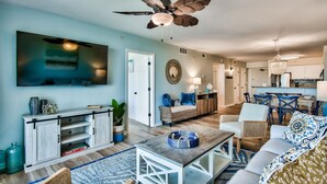 A living room with a television, sofa, coffee table, and a ceiling fan. - Luxurious Condo with Beach Access and Ocean Views (Destin)