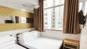 A hotel room with two beds, a wooden nightstand with shoes, a TV, and a window with curtains. - Garden Hotel (Kowloon)