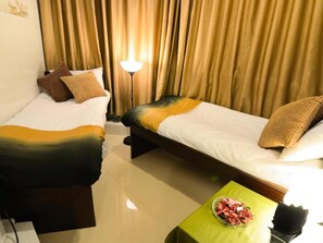 A hotel room with two beds, a nightstand, a lamp, and a bowl of snacks. - Garden Hotel (Kowloon)