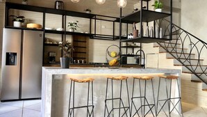 A modern kitchen with a central island, bar stools, and a staircase with a metal railing. - Casa San Antonio, Designer Villa w / Rooftop Pool. (Cartagena)