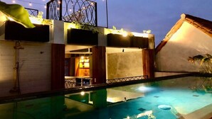 A poolside view of a building with a glass enclosure, string lights, and a balcony with plants. - Casa San Antonio, Designer Villa w / Rooftop Pool. (Cartagena)