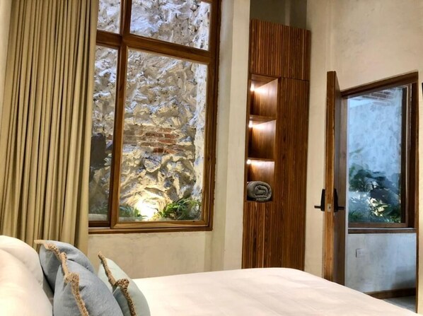 Een slaapkamer met een groot raam, een houten garderobe en een bed met kussens.