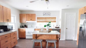 Una cocina moderna con armarios de madera, una isla central con taburetes, un refrigerador de acero inoxidable y un ventilador de techo.