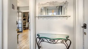 A hallway with a white door, a number '174' on the wall, a glass console table, and a decorative mirror above it.