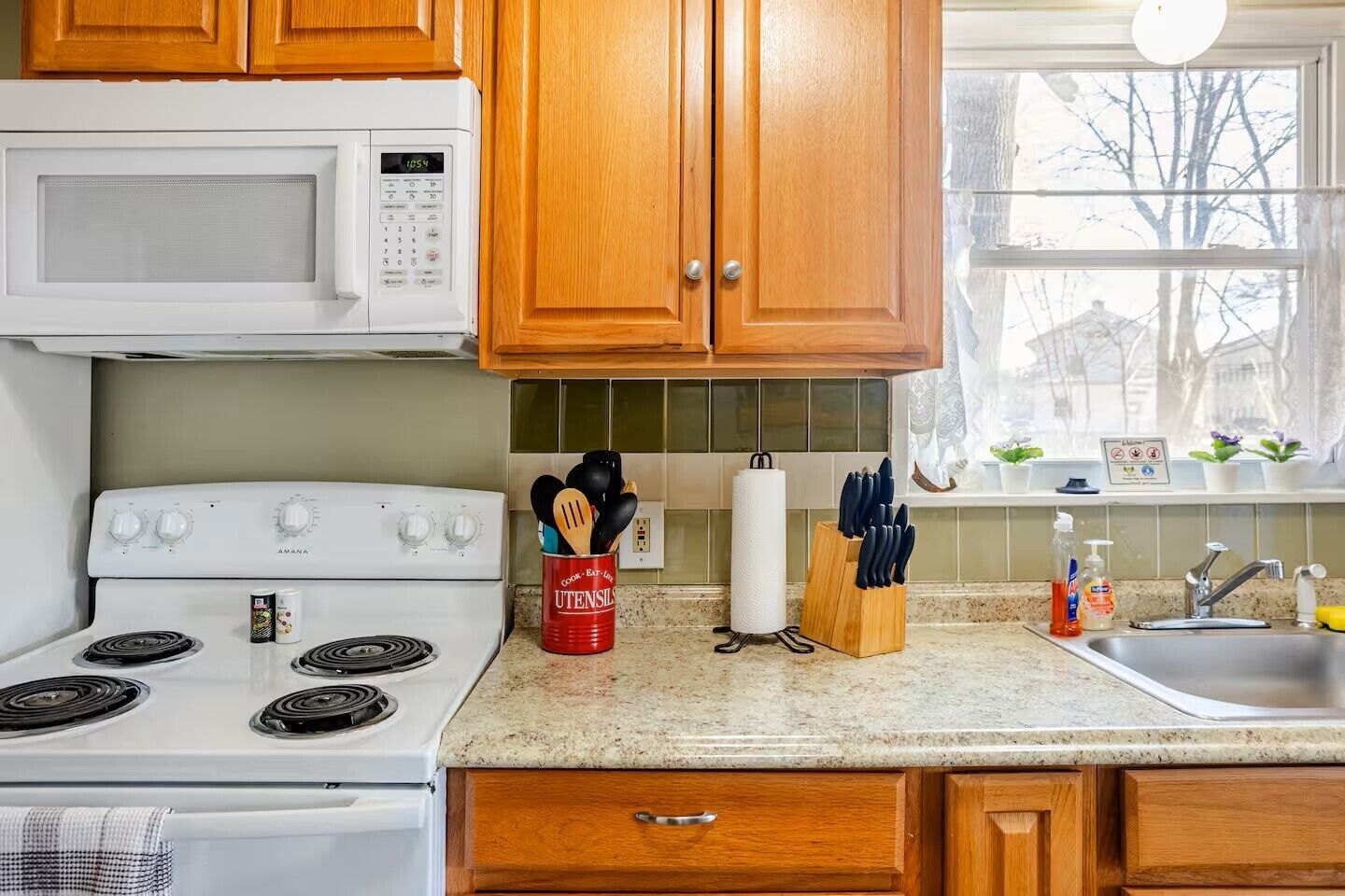 Una cocina con armarios de madera, una estufa blanca, un microondas y una ventana con vistas a árboles.
