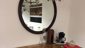 Een houten eettafel met een ronde spiegel erboven, omringd door witte stoelen met rode en witte geruite tafelkleden.