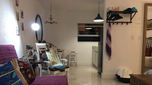 Een woonkamer met een bank, een eethoek met een tafel en stoelen, een keuken met kastjes, en een hanglamp.