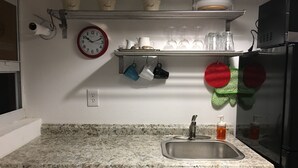 Een keuken met een granieten aanrechtblad, een roestvrijstalen spoelbak en een klok aan de muur.