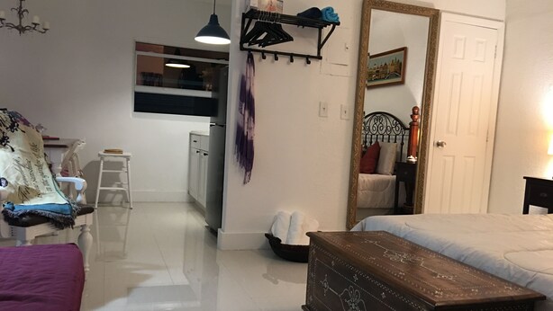 Een slaapkamer met een bed, een kaptafel en een spiegel. Er is een kleine kitchenette met een koelkast en een spoelbak.