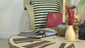 A round table with a vintage design, a wicker chair with a striped pillow, a pink bag, and decorative items. - 1 Bedroom Apt near Coconut Grove (Miami)