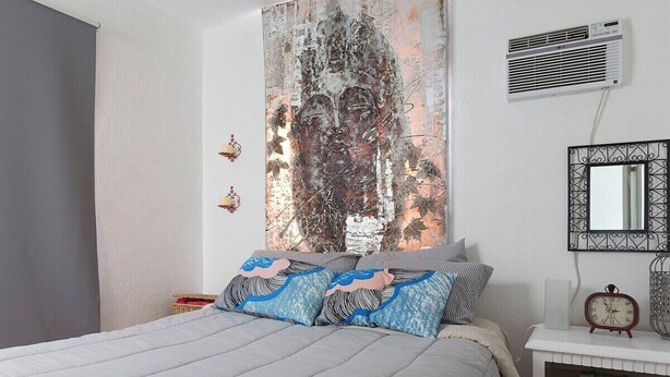 A bedroom with a bed, a wall-mounted air conditioner, a decorative mirror, and a bedside table with a clock. - 1 Bedroom Apt near Coconut Grove (Miami)