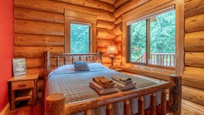 A log cabin bedroom with a bed, a nightstand, a lamp, and a sign. - Fully Loaded Lakefront Lodge w/ Pier & Game Room (Sturgeon Bay)