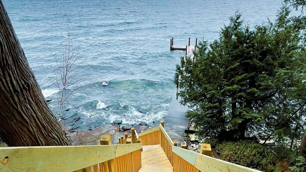 A wooden staircase leading to a beach with a view of the ocean and a cloudy sky. - Fully Loaded Lakefront Lodge w/ Pier & Game Room (Sturgeon Bay)