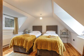 Un dormitorio con dos camas, una ventana con cortinas, una lámpara sobre una mesita de noche y un radiador.