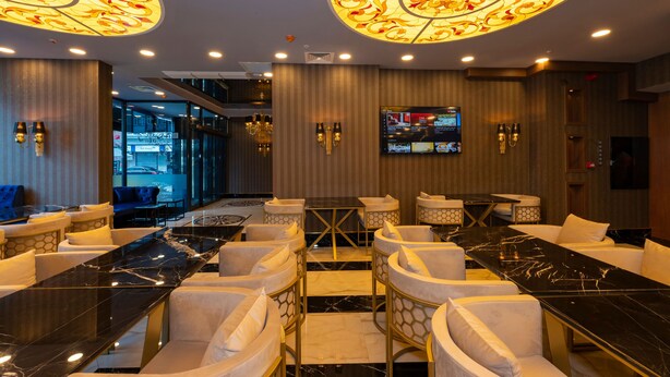A modern bar area with marble tables and white cushioned chairs, a large screen, and decorative ceiling lights. - New Emin Hotel (Istanbul)