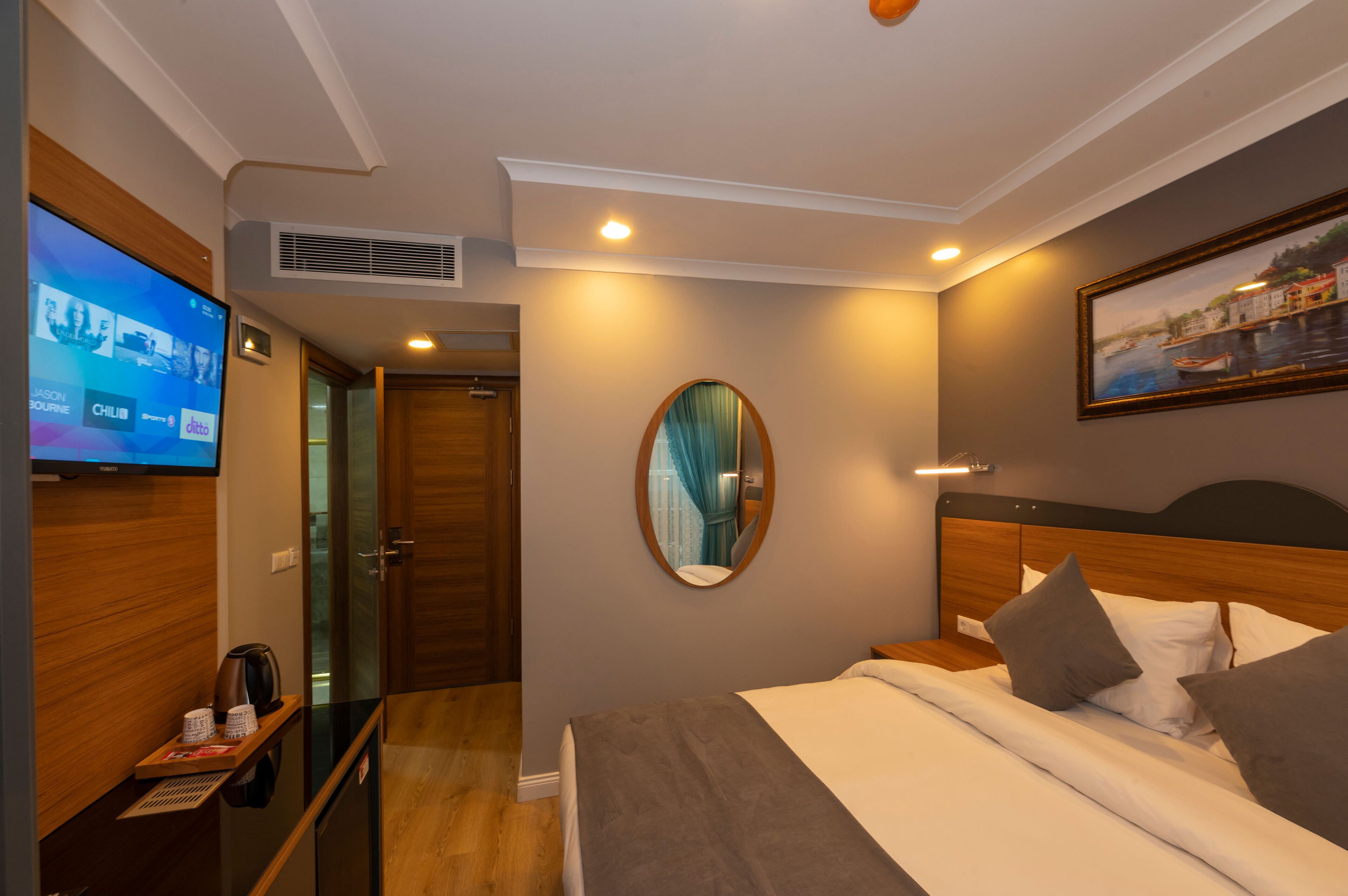 A hotel room with a bed, a TV, a mirror, and a painting on the wall.