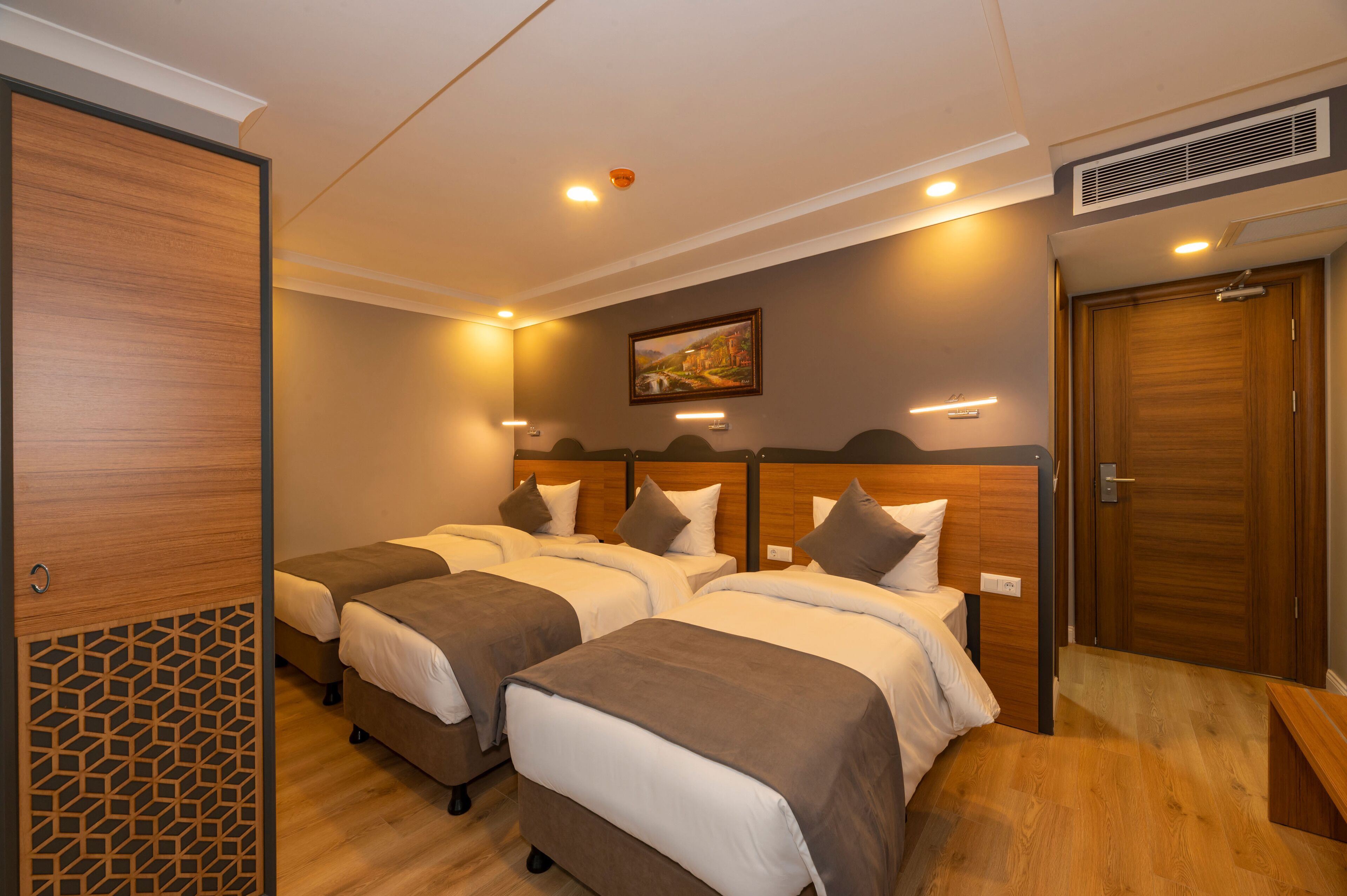 Een hotelkamer met drie bedden, houten hoofdeinden, een schilderij aan de muur en een houten deur.