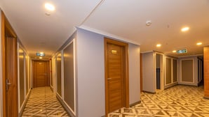 A hotel corridor with a geometric patterned floor, wooden doors, and directional signs. - New Emin Hotel (Istanbul)