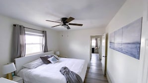 Une chambre à coucher avec un lit, un ventilateur de plafond, une table de chevet, une lampe et un tableau au mur.