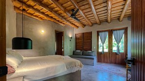 Ein Schlafzimmer mit einem großen Bett, einem Deckenventilator und Blick ins Freie durch ein Fenster.