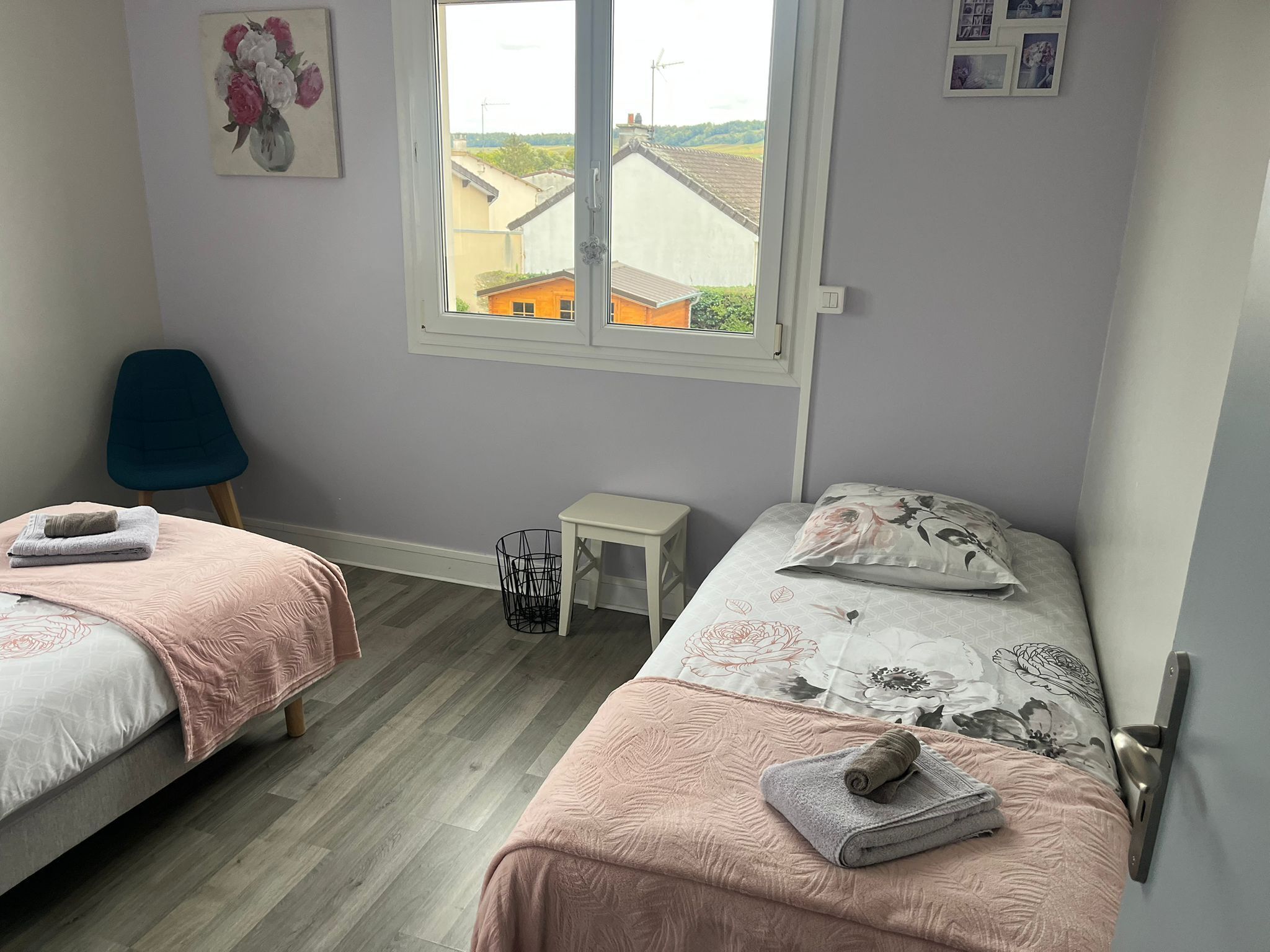 A bedroom with two beds, a window with a view of buildings, a chair, and a small table.