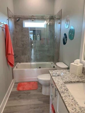 Un baño moderno con ducha de vidrio, inodoro blanco y encimera de granito.