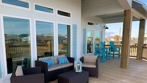 An outdoor deck with wicker furniture, a view of the ocean, and a wooden railing. - St. Somewhere, Dog Friendly (Crystal Beach)