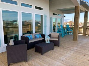 Une terrasse extérieure avec des meubles en osier, une vue sur l’océan et une rambarde en bois.