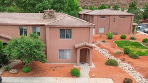 A two-story house with a stone chimney, a front door, and a small front yard with gravel and shrubs. - Spacious Townhome in Kanab! Near Zion, Bryce, and more! Pool and Hot Tub. Sleeps 8! (Kanab)