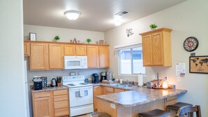 A kitchen with wooden cabinets, a microwave, a stove, a sink, and a bar area with stools. - Spacious Townhome in Kanab! Near Zion, Bryce, and more! Pool and Hot Tub. Sleeps 8! (Kanab)