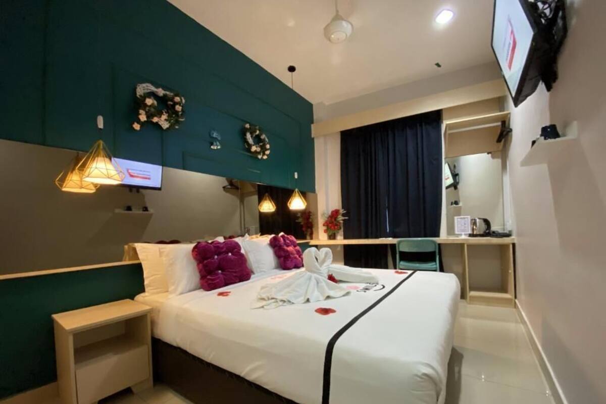A hotel room with a bed, bedside table, TV, and a desk with a chair.