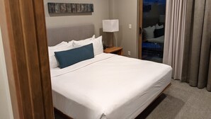A hotel room with a bed, a nightstand, a lamp, and a view of the outside through a sliding door.