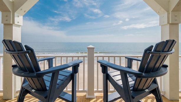 Um deck coberto com duas cadeiras Adirondack voltadas para a praia.
