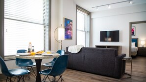 A modern living room with a grey sofa, blue chairs, a dining table with plates and a bottle, and a TV mounted on the wall. - 2 Bedroom Villa with Air-Conditioning (New Orleans)