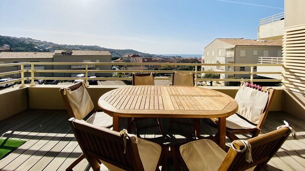 A wooden table and chairs on a balcony with a view of buildings and hills. - Les Jardins de Quatrina 2 bedrooms sea view (PROPRIANO)