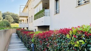 A modern building with a concrete pathway lined with vibrant red and green foliage. - Les Jardins de Quatrina 2 bedrooms sea view (PROPRIANO)