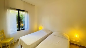 A room with two beds, a chair, and a window with curtains. - Les Jardins de Quatrina 2 bedrooms sea view (PROPRIANO)